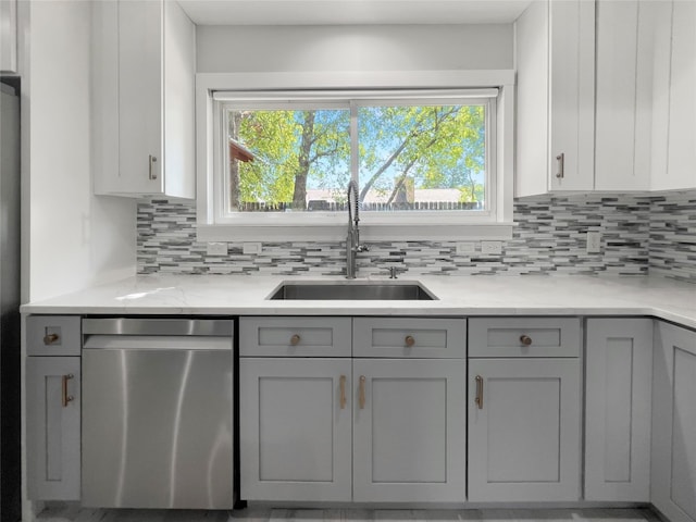 kitchen featuring stainless steel dishwasher, light stone counters, gray cabinets, and sink