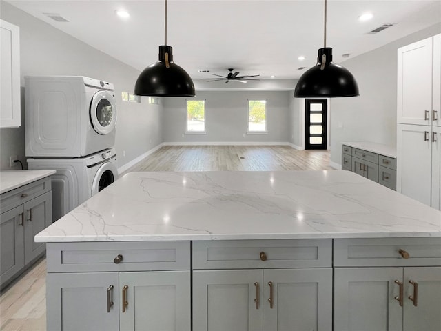 kitchen featuring ceiling fan, gray cabinetry, stacked washer / drying machine, and vaulted ceiling