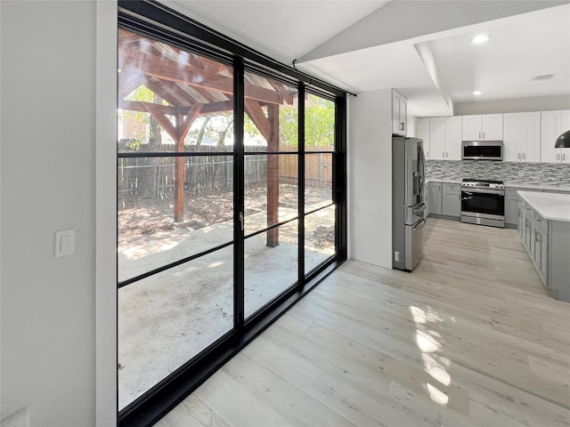 kitchen featuring gray cabinets, light hardwood / wood-style flooring, stainless steel appliances, decorative backsplash, and white cabinets