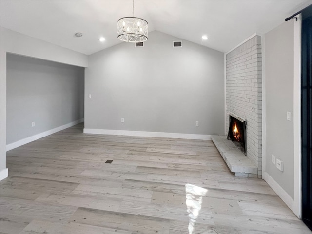 unfurnished living room featuring lofted ceiling, light hardwood / wood-style floors, a notable chandelier, and a fireplace