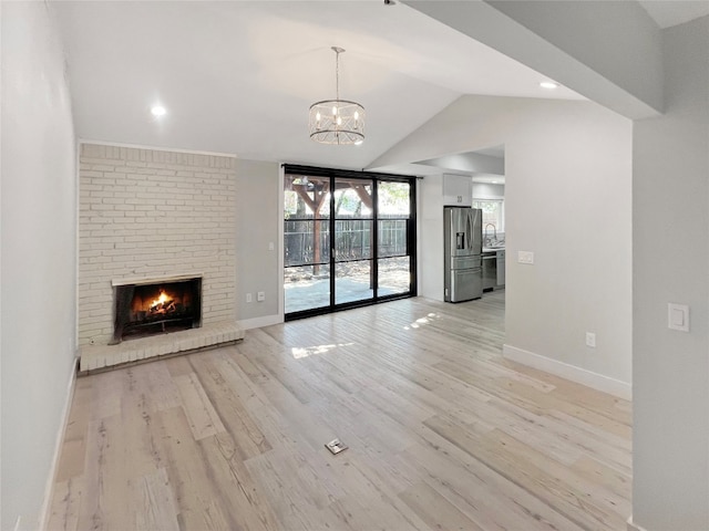 unfurnished living room with a fireplace, light hardwood / wood-style flooring, a chandelier, sink, and lofted ceiling