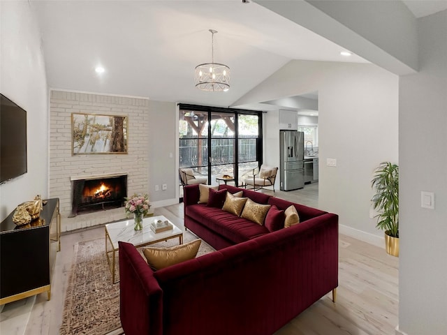 living room with a brick fireplace, light wood-type flooring, a chandelier, sink, and lofted ceiling