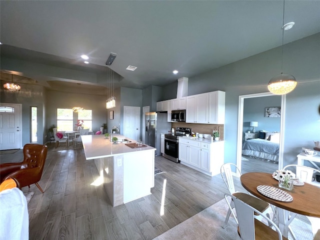 kitchen with light wood-type flooring, appliances with stainless steel finishes, white cabinetry, pendant lighting, and a center island with sink