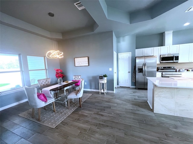 kitchen featuring pendant lighting, stainless steel appliances, a towering ceiling, a tray ceiling, and white cabinets