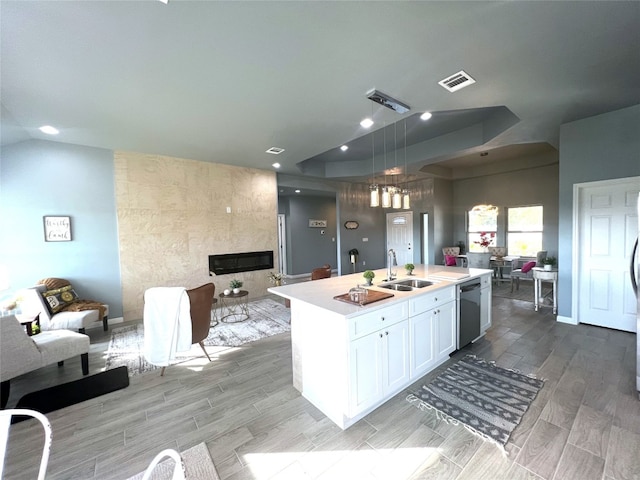 kitchen with a fireplace, dishwasher, sink, an island with sink, and white cabinets