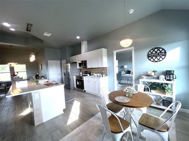 kitchen featuring white cabinetry, dark hardwood / wood-style flooring, vaulted ceiling, an island with sink, and appliances with stainless steel finishes