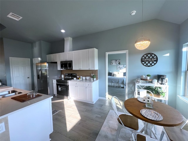 kitchen with decorative light fixtures, light hardwood / wood-style floors, stainless steel appliances, lofted ceiling, and white cabinets