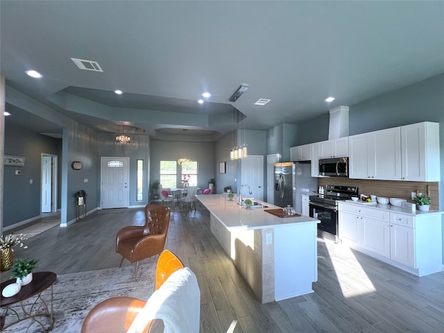 kitchen featuring white cabinets, hardwood / wood-style floors, appliances with stainless steel finishes, sink, and a kitchen island with sink