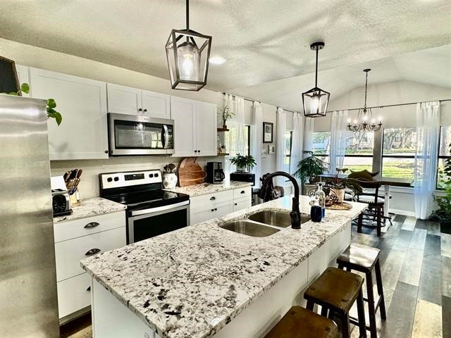 kitchen featuring white cabinetry, sink, stainless steel appliances, vaulted ceiling, and a center island with sink