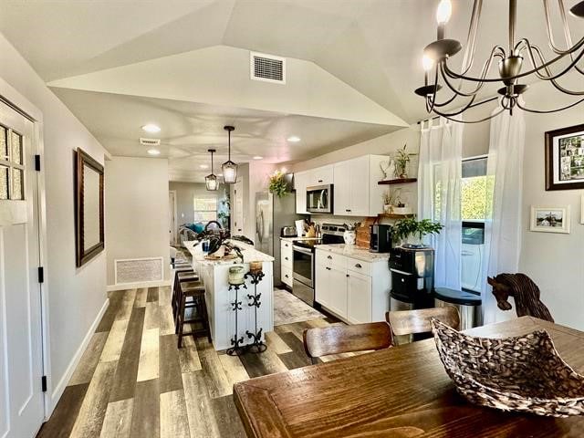 kitchen with hardwood / wood-style floors, appliances with stainless steel finishes, white cabinetry, and an island with sink