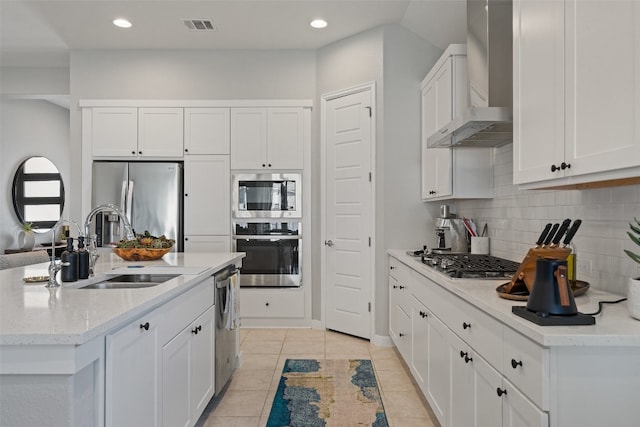 kitchen with stainless steel appliances, wall chimney exhaust hood, white cabinetry, and sink