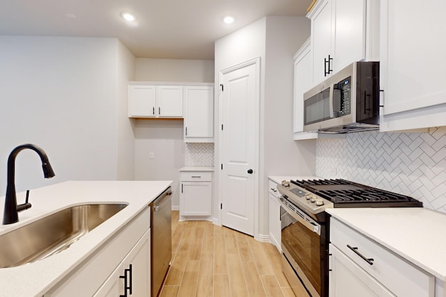 kitchen with white cabinets, sink, light wood-type flooring, tasteful backsplash, and stainless steel appliances