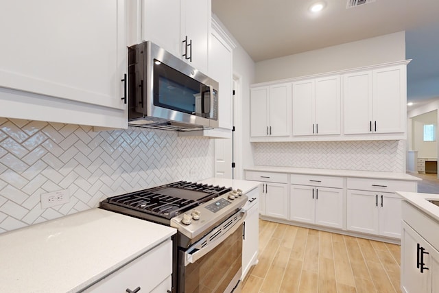 kitchen with white cabinets, appliances with stainless steel finishes, backsplash, and light hardwood / wood-style flooring