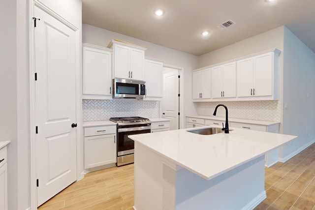 kitchen featuring white cabinets, sink, an island with sink, appliances with stainless steel finishes, and light hardwood / wood-style floors