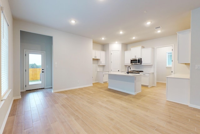 kitchen with light hardwood / wood-style flooring, white cabinetry, and a kitchen island with sink