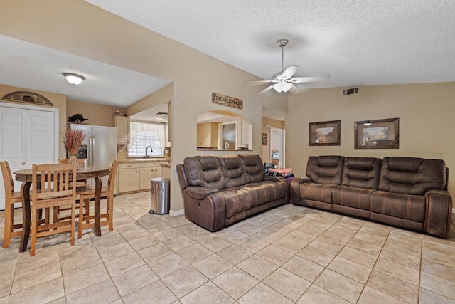 living room featuring a textured ceiling, light tile patterned floors, sink, ceiling fan, and vaulted ceiling