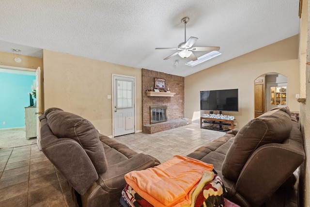 living room featuring lofted ceiling, ceiling fan, a brick fireplace, and a textured ceiling