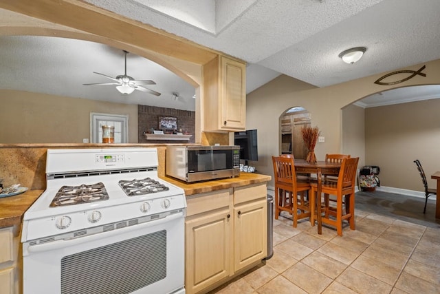 kitchen with a textured ceiling, white range with gas stovetop, lofted ceiling, ceiling fan, and light tile patterned flooring