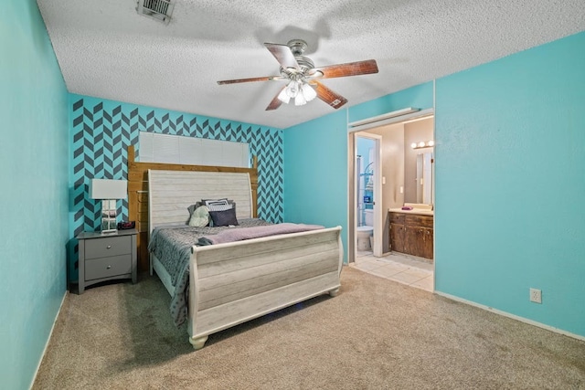 bedroom with ensuite bath, a textured ceiling, ceiling fan, and light colored carpet