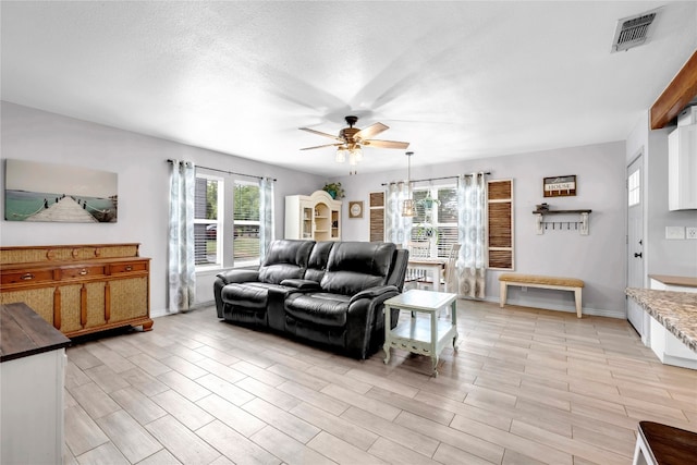 living room with a textured ceiling, ceiling fan, and light wood-type flooring