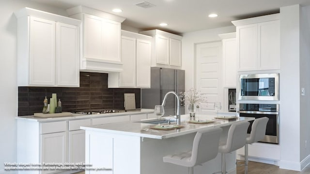 kitchen featuring stainless steel appliances, a kitchen breakfast bar, an island with sink, and white cabinets