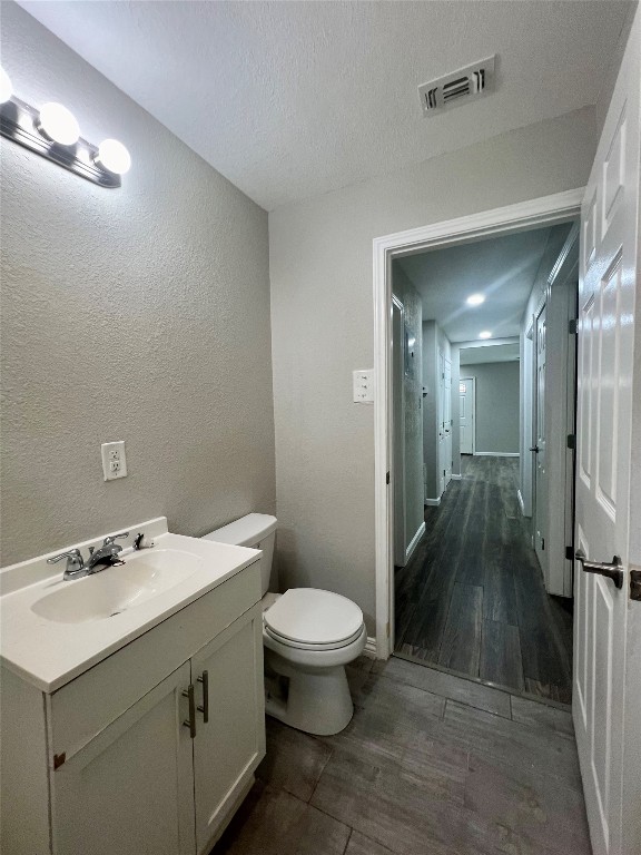 bathroom with a textured ceiling, vanity, toilet, and hardwood / wood-style flooring