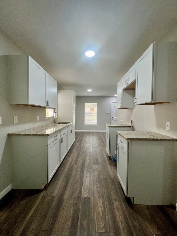 kitchen with light stone counters, sink, white cabinets, and dark hardwood / wood-style floors