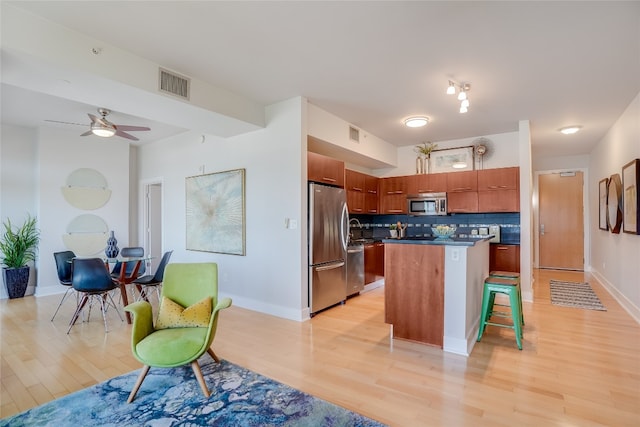 kitchen featuring a kitchen island, light hardwood / wood-style floors, a breakfast bar, stainless steel appliances, and ceiling fan