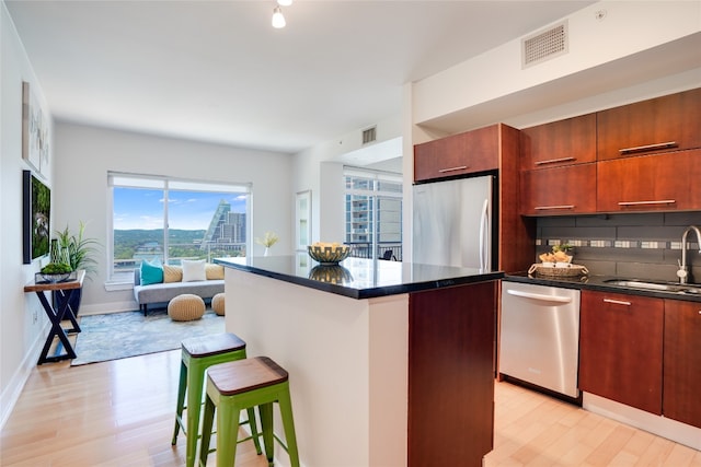 kitchen with light hardwood / wood-style flooring, backsplash, appliances with stainless steel finishes, a breakfast bar, and sink