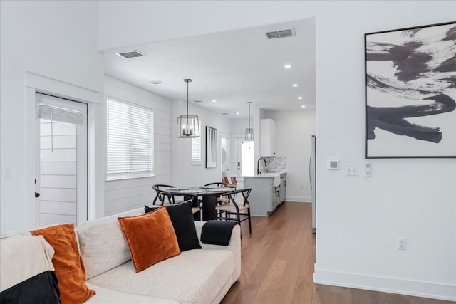 living room with sink, light wood-type flooring, and a chandelier