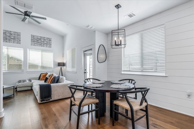 dining area with ceiling fan with notable chandelier, dark hardwood / wood-style flooring, and wood walls