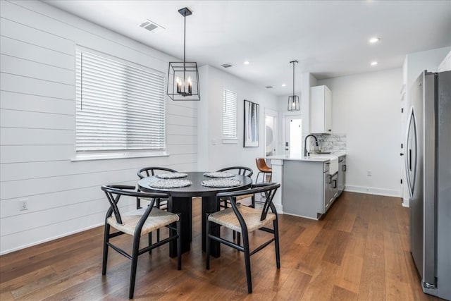 dining room with wooden walls, dark hardwood / wood-style flooring, a notable chandelier, and sink