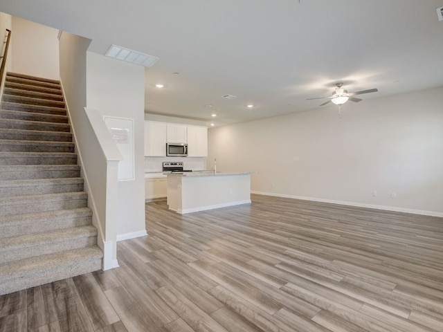 unfurnished living room featuring ceiling fan, light wood-type flooring, and sink