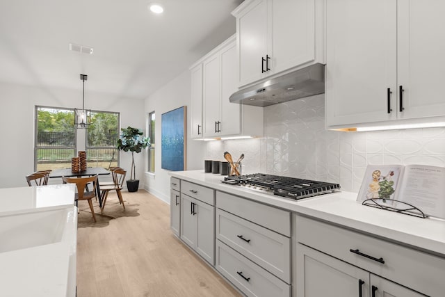 kitchen with backsplash, light hardwood / wood-style floors, stainless steel gas cooktop, white cabinets, and decorative light fixtures