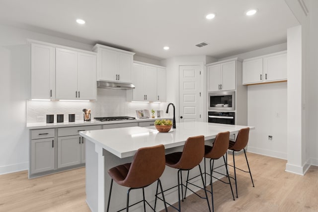 kitchen featuring light hardwood / wood-style flooring, a breakfast bar, white cabinetry, stainless steel appliances, and a center island with sink