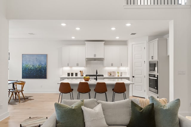 kitchen featuring appliances with stainless steel finishes, white cabinetry, backsplash, a kitchen breakfast bar, and light hardwood / wood-style floors