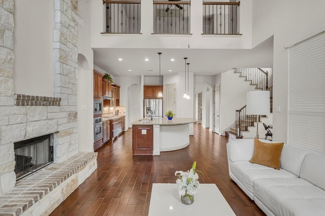 living room with sink, a towering ceiling, dark hardwood / wood-style floors, and a stone fireplace