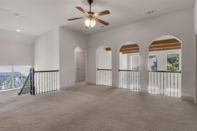 carpeted spare room with ceiling fan, beamed ceiling, and a towering ceiling