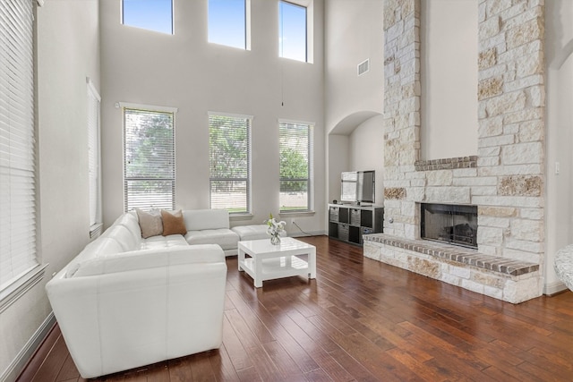 living room with a high ceiling, a stone fireplace, and dark hardwood / wood-style flooring