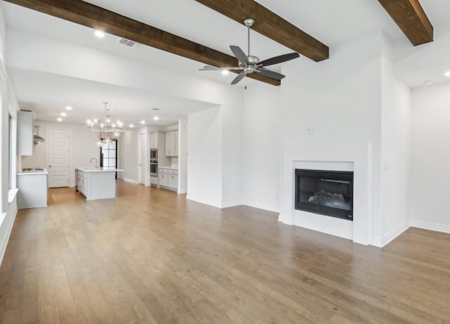 unfurnished living room with ceiling fan with notable chandelier, sink, beam ceiling, and light hardwood / wood-style floors