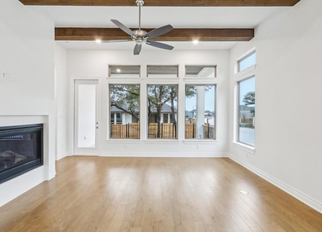 unfurnished living room featuring beamed ceiling, ceiling fan, a healthy amount of sunlight, and light wood-type flooring