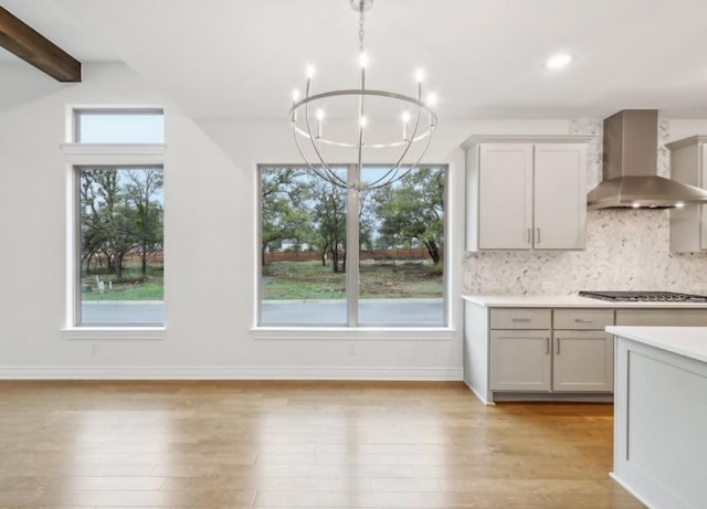 kitchen with stainless steel gas cooktop, gray cabinetry, pendant lighting, decorative backsplash, and wall chimney range hood