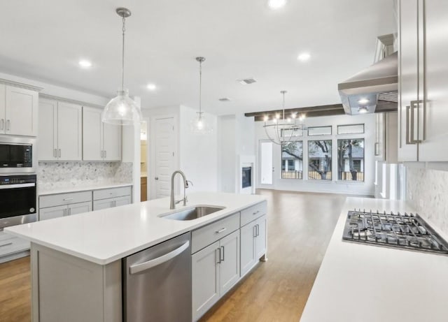 kitchen featuring hanging light fixtures, appliances with stainless steel finishes, sink, and a kitchen island with sink