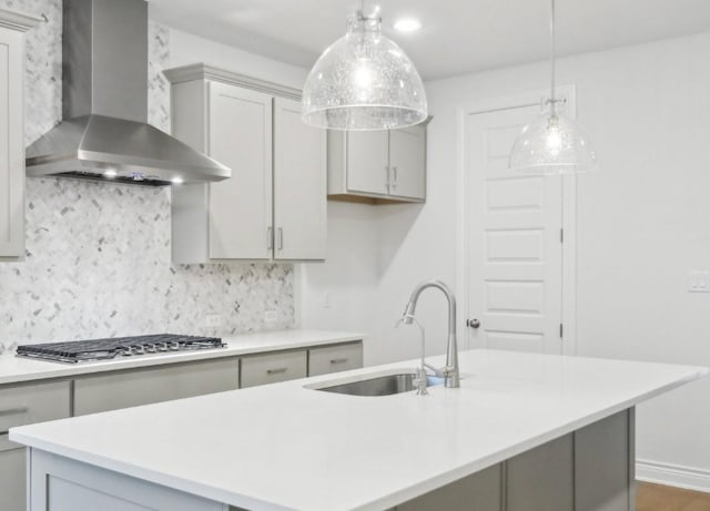 kitchen featuring stainless steel gas stovetop, sink, gray cabinetry, and wall chimney exhaust hood