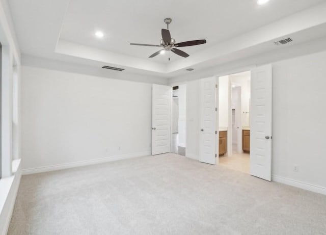 unfurnished bedroom with light colored carpet, connected bathroom, and a tray ceiling