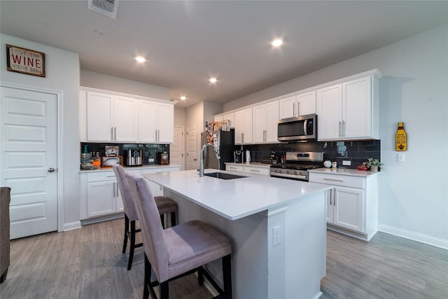 kitchen with appliances with stainless steel finishes, light hardwood / wood-style floors, white cabinetry, an island with sink, and sink