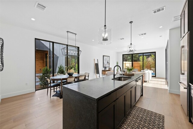 kitchen featuring hanging light fixtures, sink, light hardwood / wood-style flooring, and an island with sink