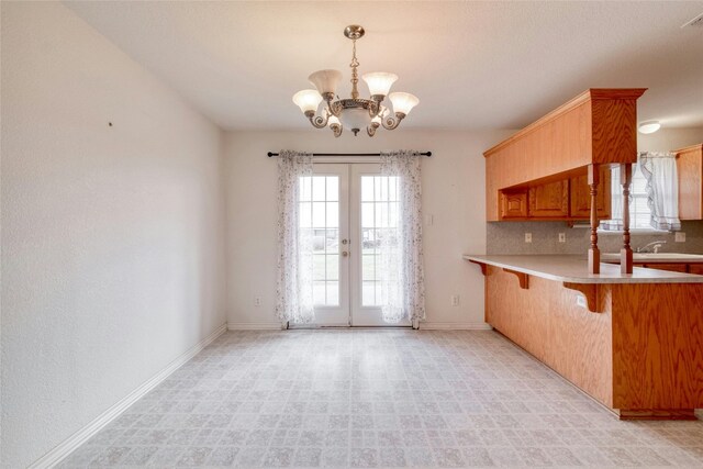 kitchen with pendant lighting, kitchen peninsula, tasteful backsplash, a kitchen breakfast bar, and a notable chandelier