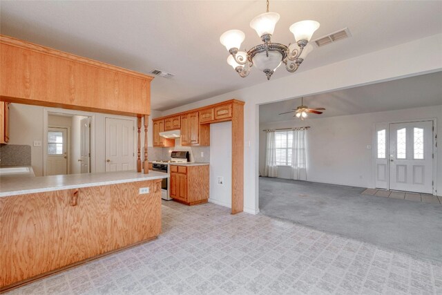 kitchen featuring ceiling fan with notable chandelier, kitchen peninsula, decorative light fixtures, light colored carpet, and stainless steel range