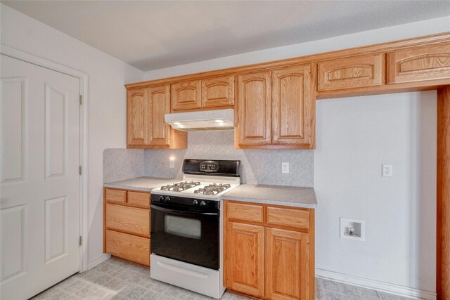 kitchen featuring light brown cabinetry, backsplash, and white gas range